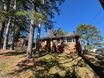 Charming single-story brick house with a welcoming front porch and landscaped yard surrounded by mature trees at 1220 Roanoke Ave, Henderson, NC 27536