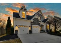 Charming home showcasing a three car garage and stone accents against a vibrant sunset backdrop at 2505 Mt Zion Church Rd Rd, Apex, NC 27502