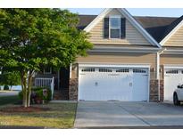 Inviting townhouse featuring a two-car garage, manicured lawn, and stone accents at 63 Radcliffe Ct, Clayton, NC 27527