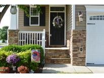 Charming home entrance with stone accents, a wreath, and potted plants for inviting curb appeal at 63 Radcliffe Ct, Clayton, NC 27527