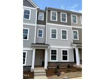 View of townhomes featuring neutral color palettes, stone accents, and ample windows under a partly cloudy sky at 3011 Honeymyrtle Ln, Durham, NC 27703