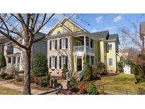Charming two-story home with yellow siding, brick accents, black shutters, and a welcoming double-decker porch at 10319 Evergreen Spring Pl, Raleigh, NC 27614