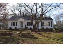 Charming white home with black shutters, mature trees, and a picnic table on a sunny day at 1110 S Second Ave, Siler City, NC 27344