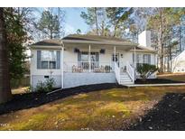 Charming home featuring a cozy front porch with lovely hanging floral arrangements and manicured landscaping at 224 Round About Rd, Holly Springs, NC 27540