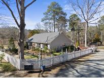 Charming home featuring a white picket fence, lush landscaping, and a serene, tree-filled setting at 8809 Farrington Mill Rd, Chapel Hill, NC 27517