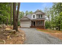 Charming two-story home featuring a gravel driveway, attached garage, and welcoming front porch nestled among mature trees at 5507 Eagles Nest Trl, Snow Camp, NC 27349