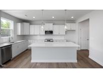 Bright kitchen features white cabinets, an island with quartz countertop, and stainless steel appliances at 173 Wild Turkey Way, Lillington, NC 27546