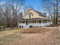 Inviting yellow two-story home featuring a wraparound porch and mature landscaping at 7132 Linda Rae Dr, Zebulon, NC 27597