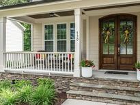 Inviting front porch with stone base, white columns, and a lovely arched wood front door with glass and decorative wreaths at 730 Toms Creek Rd, Cary, NC 27519