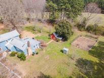 A charming blue home with a metal roof, sheds, and a fenced area is surrounded by lush greenery at 1024 Tobacco Rd, Pittsboro, NC 27312