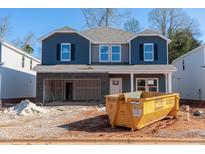 Two-story home showcasing a blue and gray exterior, a partially completed garage, and a construction dumpster at 165 Klamath Dr, Garner, NC 27529