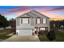Charming two-story home with gray siding, stone accents, and a two-car garage, set against a vibrant sunset sky at 201 Oakton Ridge Pl, Garner, NC 27529