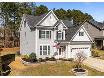 Charming two-story home with a manicured lawn, a two-car garage, and a welcoming front porch with an American flag at 104 Vinewood Pl, Holly Springs, NC 27540