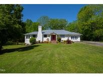 Charming white brick home with a red front door, manicured lawn, and lush landscaping on a sunny day at 513 N Nash St, Hillsborough, NC 27278