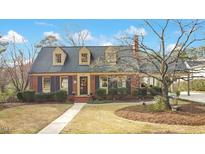 Charming brick home featuring dormer windows, manicured landscaping, and mature trees at 527 N Main St, Wake Forest, NC 27587