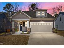 Charming home featuring a two-car garage, stone accents, and lovely landscaping at dusk at 5212 Huntley Overlook Dr, Durham, NC 27703