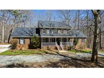 Charming brick home with a welcoming front porch, set amongst a wooded landscape and blue skies at 1500 Allen Ln, Hillsborough, NC 27278