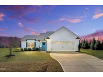 Beautiful, white single-story home with a large garage and a well-manicured lawn underneath a dramatic sky at 28 Sandcastle Ln, Four Oaks, NC 27524