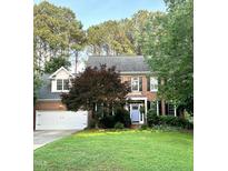 Charming two-story brick home featuring a manicured lawn, lush trees and a delightful periwinkle front door at 307 Kellyridge Dr, Apex, NC 27502