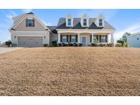 Inviting two-story home featuring dormer windows, covered porch, attached garage, and lawn on a sunny day at 21 Tracker Ct, Garner, NC 27529