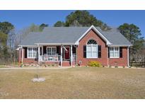 Charming red brick home featuring a cozy front porch with white railing and rocking chairs at 703 E Stanley St, Four Oaks, NC 27524