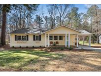 Charming yellow single-story home featuring a covered front porch, a carport, and a well-maintained front yard at 135 Windsor Cir, Chapel Hill, NC 27516