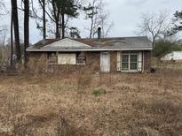 Single-story brick home with covered front entrance surrounded by overgrown grass in need of landscaping at 5001 Royal Acres Rd, Raleigh, NC 27610
