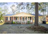 Charming brick home with a welcoming front porch and white railing, complemented by lush greenery and a sunlit backdrop at 626 S Hollybrook Rd, Wendell, NC 27591