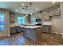 Modern kitchen boasts gray cabinetry, stainless steel appliances, a center island with white countertops, and stylish pendant lighting at 607 Callan View Ave, Wake Forest, NC 27587