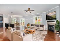 Bright living room featuring a fireplace, hardwood floors, ceiling fan, and an open floor plan with access to the kitchen at 101 Lager Ln, Garner, NC 27529