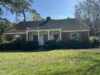 Charming brick home with a covered front porch, blue shutters, and a spacious, overgrown front lawn at 1101 W Divine St, Dunn, NC 28334