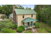 Charming yellow home with a green metal roof, brick chimney, and inviting front porch with blue chairs at 2409 Hodges Rd, Burlington, NC 27217