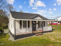 Charming home featuring a cozy front porch, a dark roof and black shutters accenting the bright white exterior at 315 Cates Ave, Burlington, NC 27215
