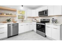 Bright kitchen with white cabinets, stainless steel appliances, and floating wood shelves at 1409 Ida St, Durham, NC 27705