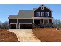 New two-story home featuring a three-car garage and a charming front porch with stone accents at 4893 Grosbeak Ct, Mebane, NC 27302