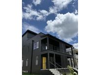Contemporary black home featuring a yellow front door, complemented by a blue sky with puffy white clouds at 409 Alston St # 102, Raleigh, NC 27601