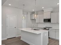Bright kitchen features an island, stainless appliances, pendant lights, and white cabinetry at 303 Old Fashioned Way, Lillington, NC 27546