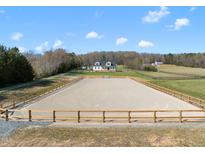 Expansive equestrian arena with wood perimeter fencing and a beautiful white farmhouse in the background on a sunny day at 2142 Henderson Tanyard Rd, Pittsboro, NC 27312