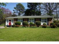 Charming brick home with a manicured front yard, trimmed shrubs and a vibrant red front door at 3516 Apache Dr, Raleigh, NC 27609