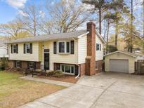 Charming split-level home featuring a brick chimney, black shutters and an inviting driveway leading to a detached garage at 6216 Lewisand Cir, Raleigh, NC 27615