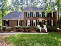 Charming brick home featuring black shutters, a manicured lawn, and mature trees, creating a welcoming curb appeal at 100 Lochberry Ln, Cary, NC 27518