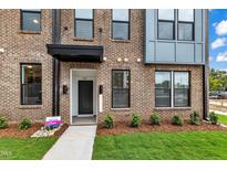 Modern townhome entrance with brick facade, manicured lawn, and visible unit number at 1234 Coach Station Alley # 101, Raleigh, NC 27601
