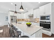 Bright kitchen boasts white cabinets, stainless steel appliances, and a large island with seating at 11549 Helmond Way # 116, Raleigh, NC 27617