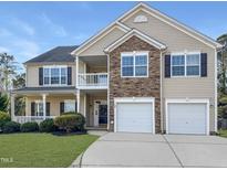 Charming two-story home featuring a stone facade, two-car garage, second story balcony, and landscaped front yard at 120 Wellspring Dr, Holly Springs, NC 27540