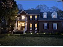 Charming two-story brick home featuring a balcony, dormer windows, and manicured lawn at twilight at 8508 Kayenta Ct, Wake Forest, NC 27587