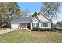 Charming single-story home boasts a well-manicured lawn, cozy front porch, and attached garage, perfect for suburban living at 105 Damask Rose Dr, Holly Springs, NC 27540