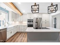 Bright kitchen featuring white cabinets, stainless appliances, island with cooktop, and modern lighting at 4012 Old Sturbridge Dr, Apex, NC 27539