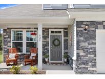 Charming front porch features stone accents, gray front door with wreath, and rocking chairs at 825 Golden Plum Ln, Zebulon, NC 27597