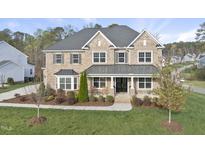 Elegant two-story brick home featuring a covered front porch, manicured lawn, and symmetrical window placement at 8117 Fergus Ct, Wake Forest, NC 27587
