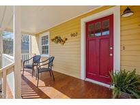 Inviting front porch featuring hardwood floors, stylish seating, and a vibrant red front door at 907 Carolina Ave, Durham, NC 27705